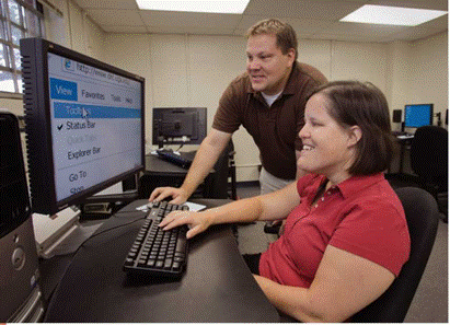 A male teacher is showing a female student on a computer that you can zoom in on anything on your monitor so it will be easier to read.