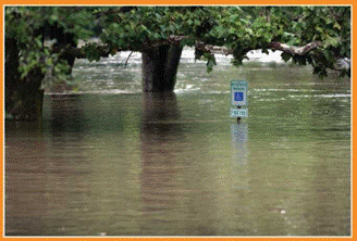 A flooded parking lot with only the top of a signpost and a tree showing above the water line.